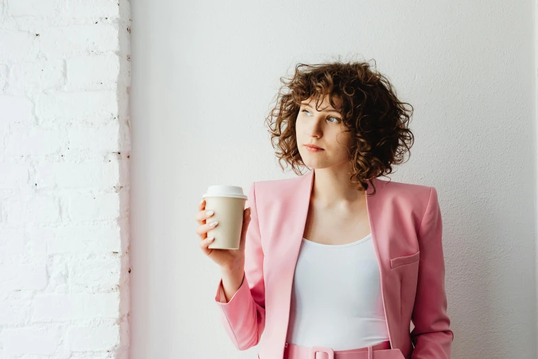 a woman in a pink suit holding a cup of coffee, by Nicolette Macnamara, trending on pexels, renaissance, curly brown hair, looking off into the distance, paper cup, attractive androgynous humanoid