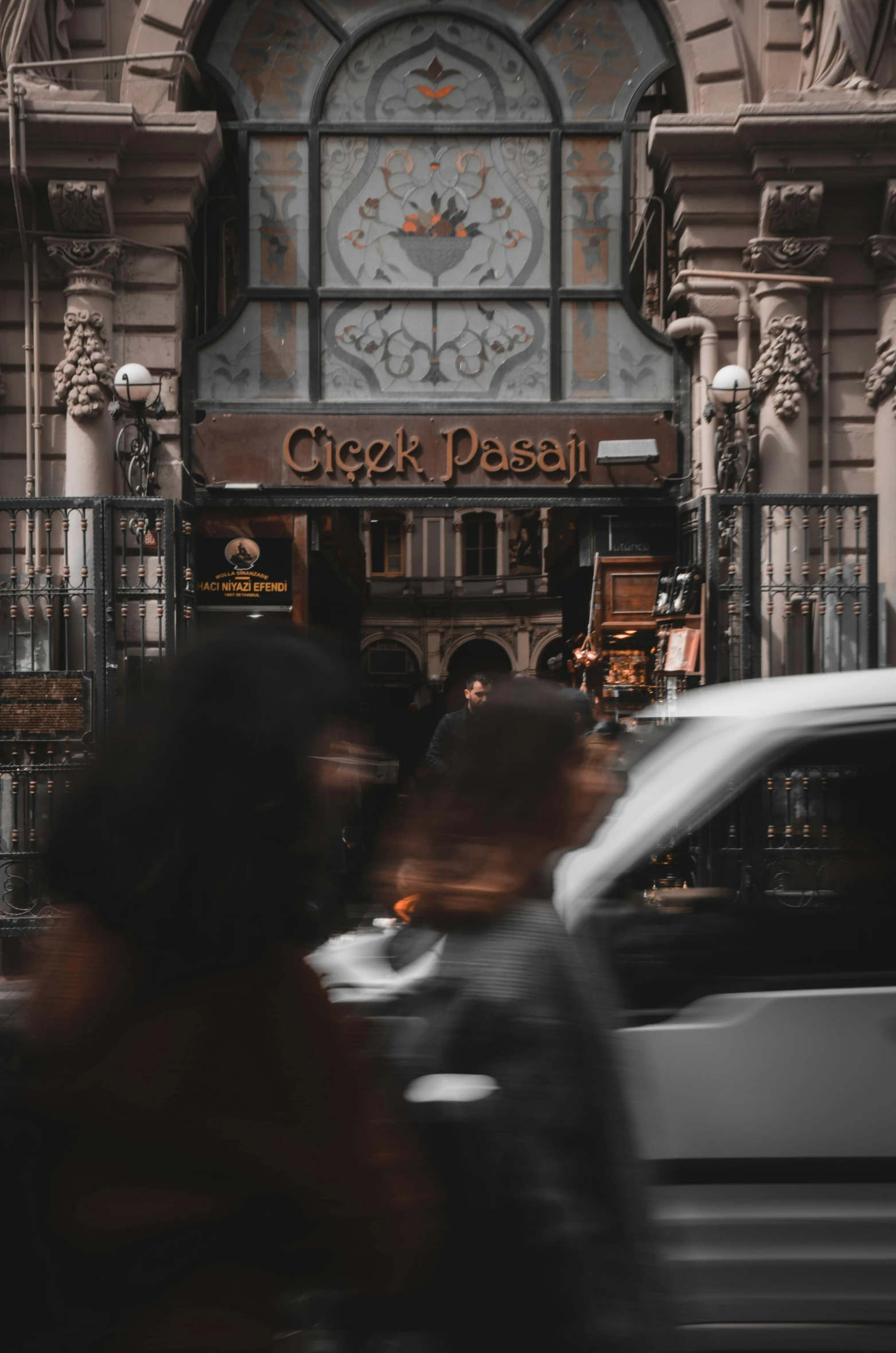 a group of people standing in front of a building, by Gusztáv Kelety, pexels contest winner, art nouveau, driving through the city, exiting store, turkish and russian, grey