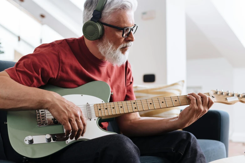 a man sitting on a couch playing a guitar, inspired by John McLaughlin, trending on pexels, old gigachad with grey beard, a green, red sunglasses and a guitar, australian