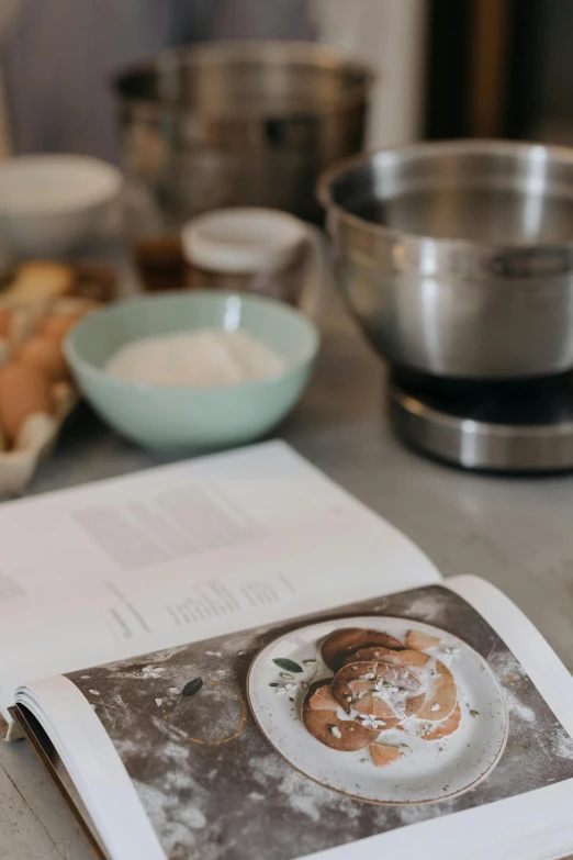 a cookbook sitting on top of a wooden table, a still life, trending on pexels, baking cookies, stainless steel, low quality photo