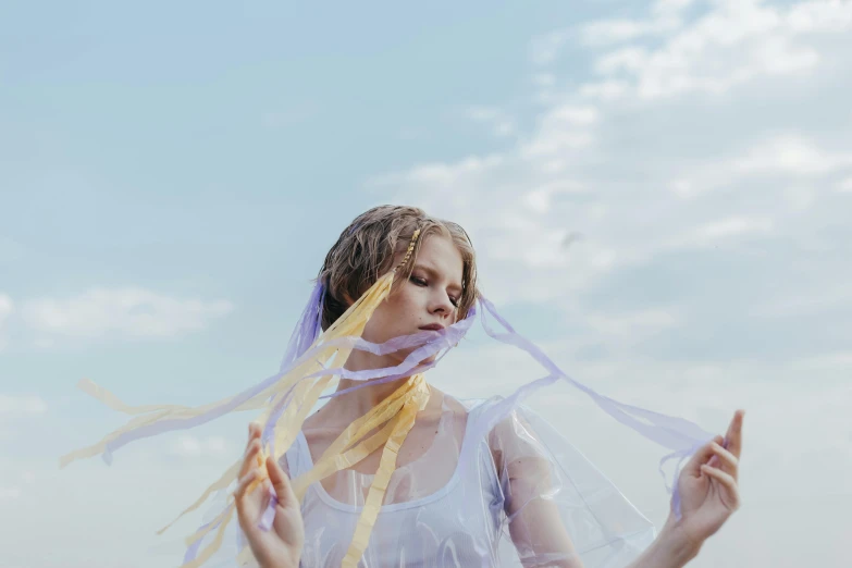 a woman standing on top of a lush green field, an album cover, inspired by Ren Hang, pexels contest winner, aestheticism, blue and yellow ribbons, white transparent veil, taylor swift made of purple ice, sydney sweeney