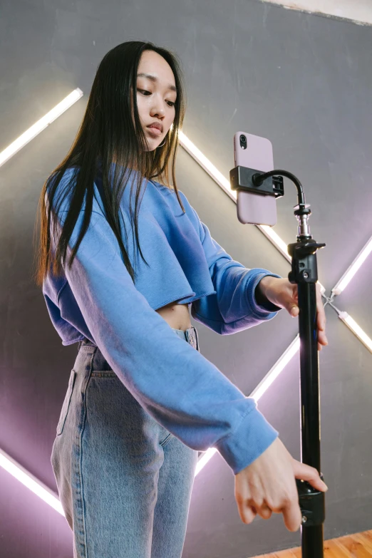 a woman standing in front of a camera on a tripod, trending on pexels, holding a blue lightsaber, phone photo, wearing a crop top, a young asian woman