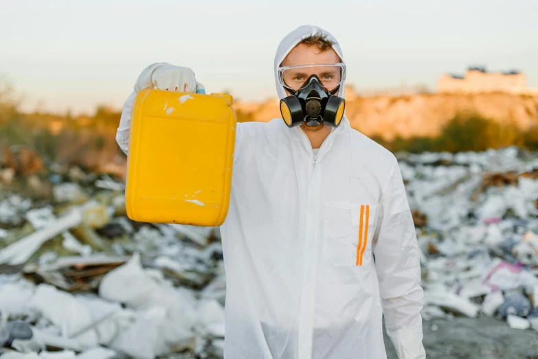 a man in a white hazmat suit holding a yellow container, pexels contest winner, wearing ripped dirty flight suit, avatar image, landfill, tourist photo