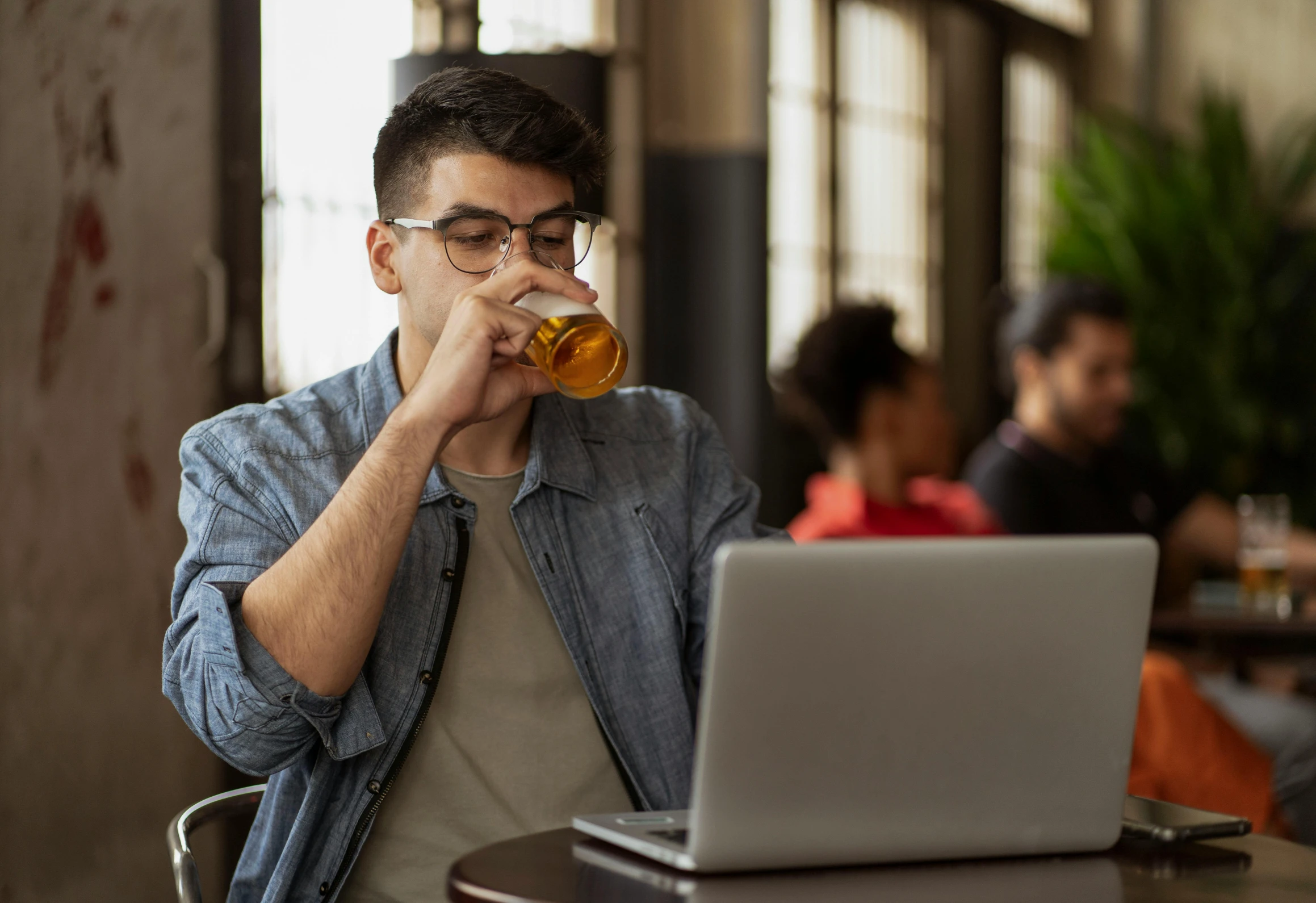 a man sitting in front of a laptop drinking a beer, by Carey Morris, pexels, renaissance, aboriginal australian hipster, at college, thick rimmed glasses, a handsome