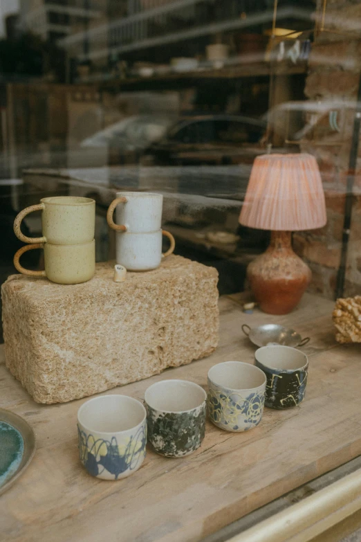 a couple of cups sitting on top of a wooden table, shop front, lamps, variety of shapes and textures, thumbnail