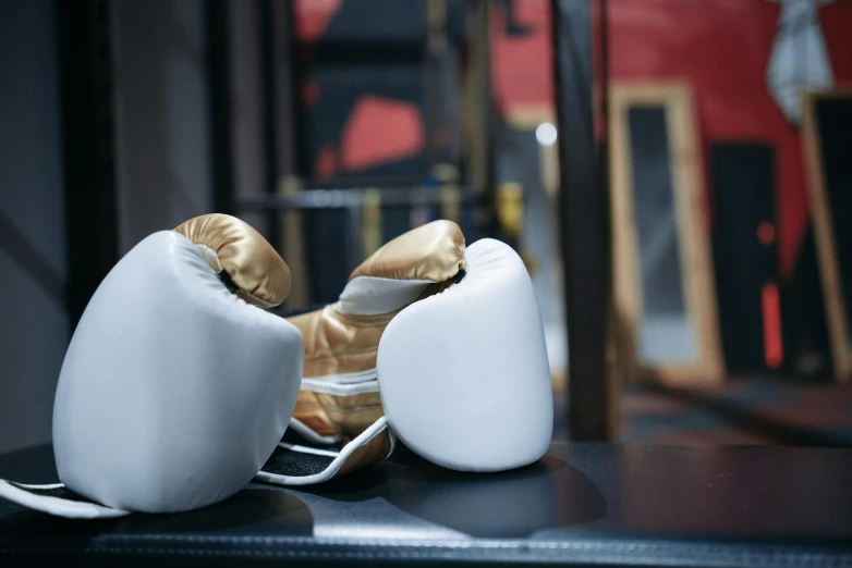 a pair of boxing gloves sitting on top of a table, gold and white, dingy gym, thumbnail, head down