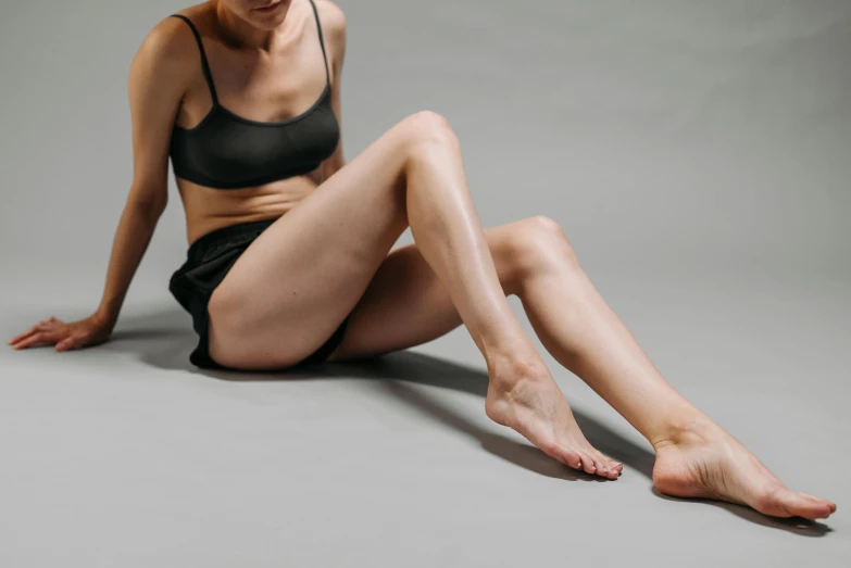 a woman sitting on the floor with her legs crossed, trending on pexels, hyperrealism, muscles, on a gray background, tans, upper and lower body