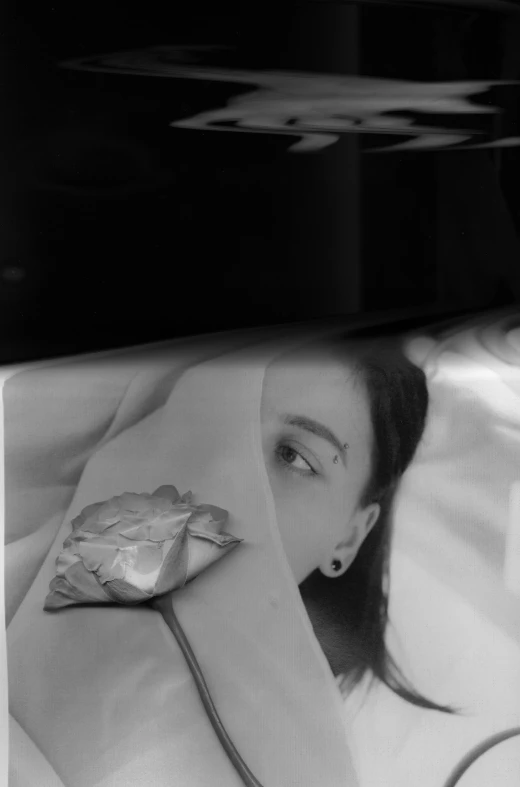 a black and white photo of a woman laying in bed, inspired by Arnold Newman, photorealism, reflecting flower, in plastic, face with artgram, still from a music video