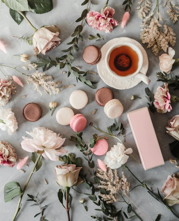 a cup of tea surrounded by flowers and macaroons, inspired by Eden Box, trending on unsplash, pink scheme, charcoal and champagne, desserts, on grey background