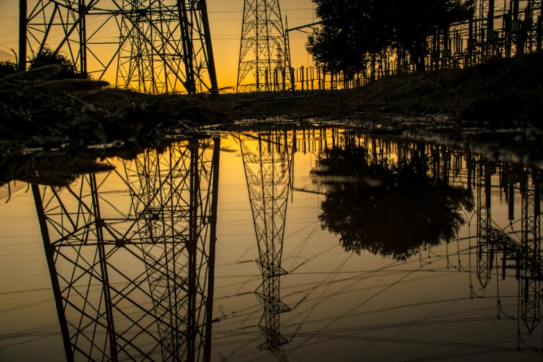 a body of water with power lines in the background, unsplash contest winner, reflective ground, silhouetted, disaster photography, orange electricity