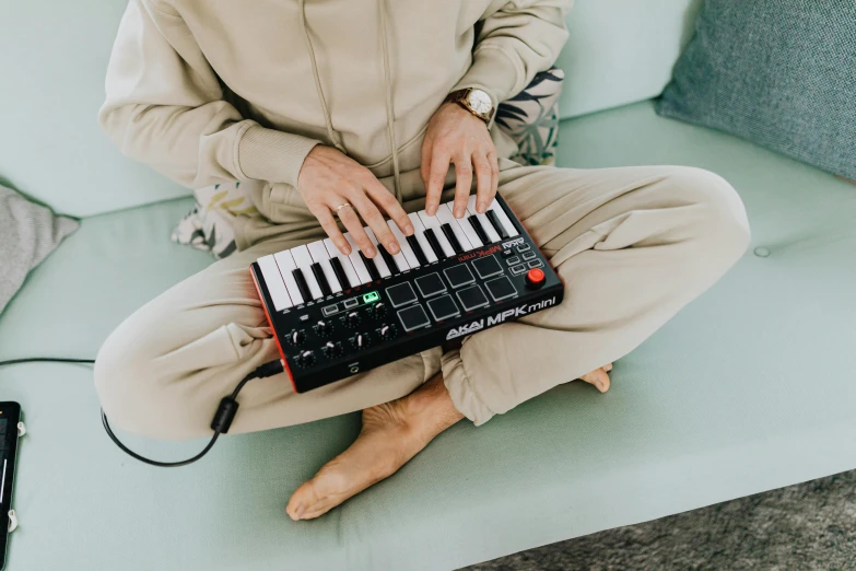 a person sitting on a couch with a keyboard, an album cover, by Julia Pishtar, trending on pexels, holding controller, chappie in an adidas track suit, ergodox, music instruments