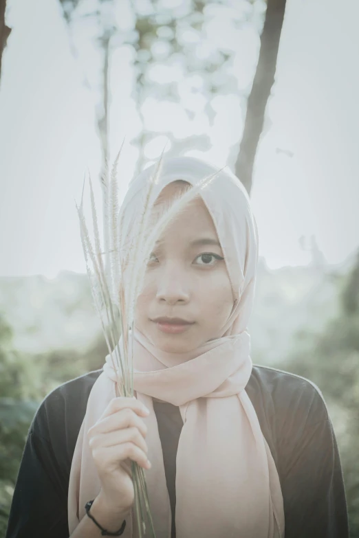 a woman in a hijab holding a bunch of grass, unsplash, hurufiyya, medium format. soft light, ((portrait)), asian face, desaturated