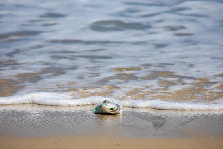 a bottle sitting on top of a beach next to the ocean, barreleye, in the water, flattened, mother of pearl jewelry