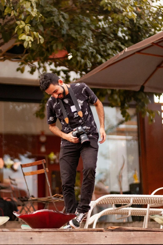 a man that is standing on a skateboard, by Ismail Acar, happening, holding a dslr camera, standing in a restaurant, patterned, wearing a shirt