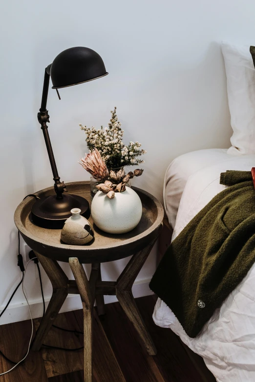 a bed room with a neatly made bed, a still life, by Robbie Trevino, trending on unsplash, romanticism, vase with flowers, lamp, detailed product shot, angled shot