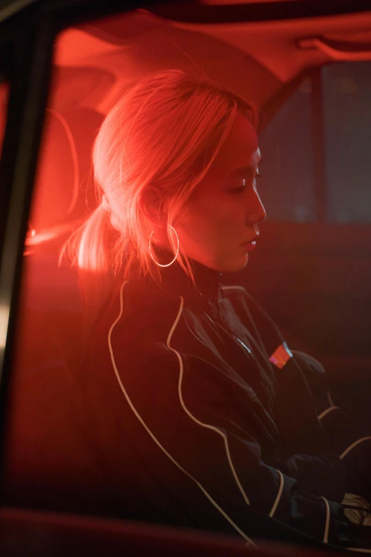 a woman sitting in the passenger seat of a car, inspired by Nan Goldin, trending on pexels, black and red jacket, jamie chung, kiko mizuhara, orange neon backlighting