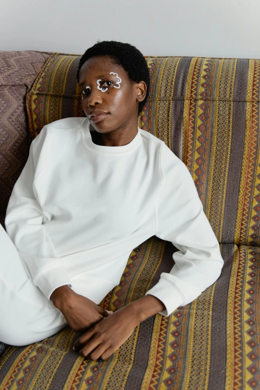 a woman sitting on a couch with her legs crossed, inspired by Sarah Lucas, trending on pexels, wearing a track suit, wearing a white sweater, dark skinned, wearing a patch over one eye