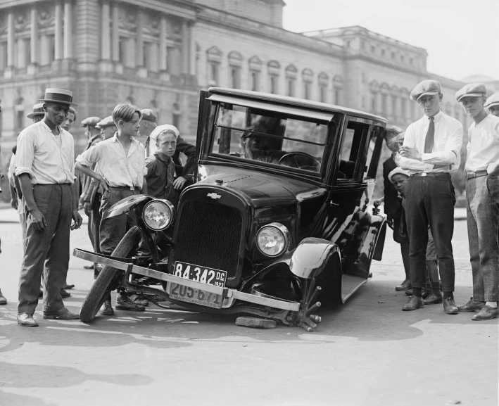 a group of men standing around an old car, by Maurycy Gottlieb, pixabay, traffic accident, square, 1920s picture, a boy