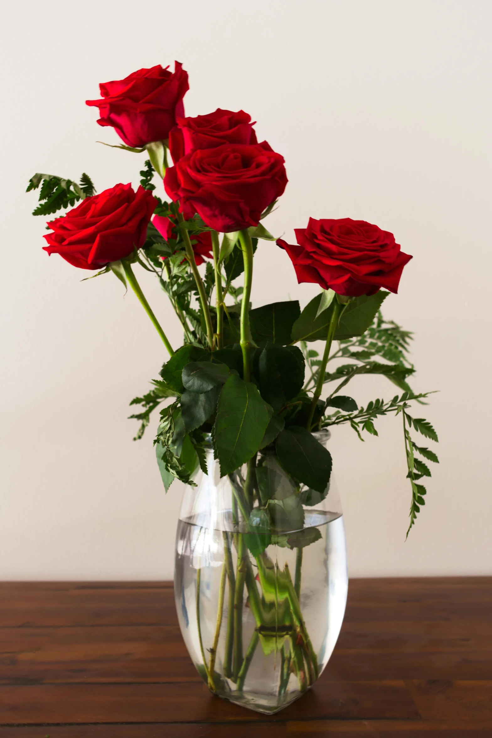 a vase filled with red roses sitting on a table, visually crisp & clear, award winning seductive, minimalist, in a short round glass vase