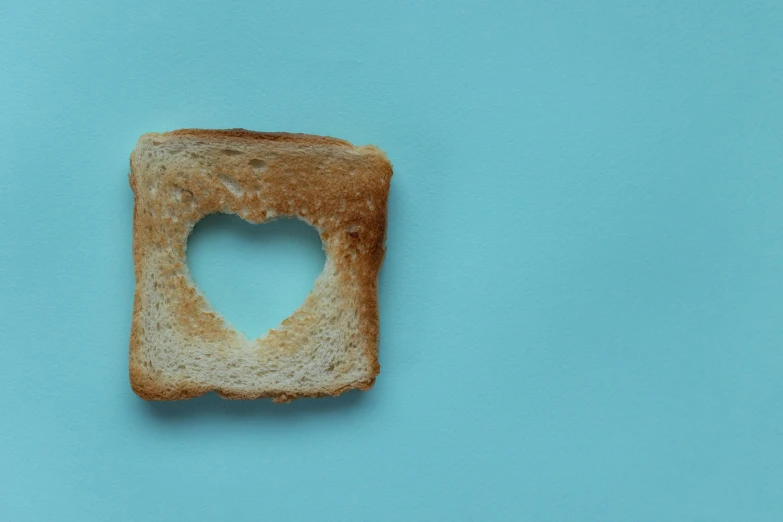 a piece of bread with a heart cut in it, by Sylvia Wishart, trending on pexels, postminimalism, with a blue background, toast, with a square, halo halo halo halo 8k