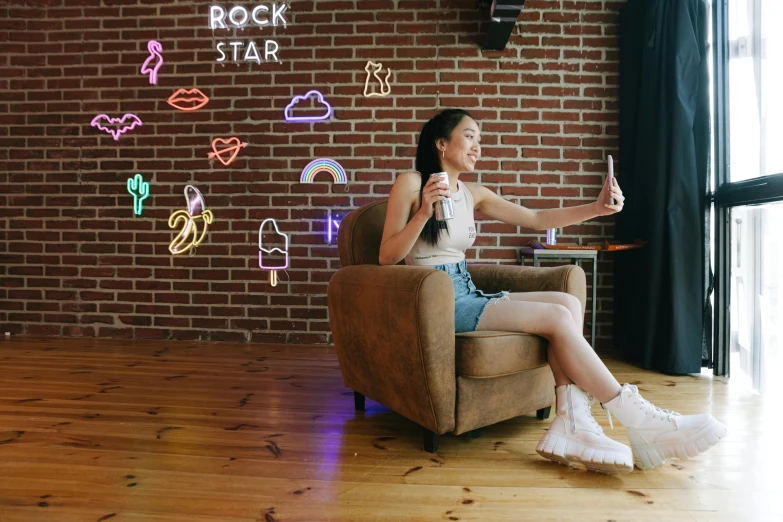 a woman sitting in a chair in front of a brick wall, a hologram, trending on pexels, interactive art, teenager hangout spot, taking selfies, rock star, neon standup bar