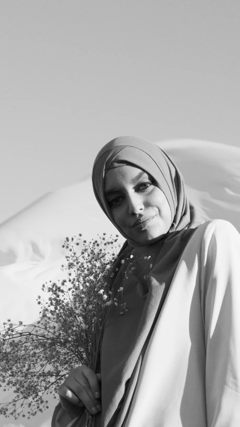 a black and white photo of a woman with a bouquet of flowers, inspired by Maryam Hashemi, hurufiyya, wearing white silk hood, 15081959 21121991 01012000 4k, in front of an orange background, dune