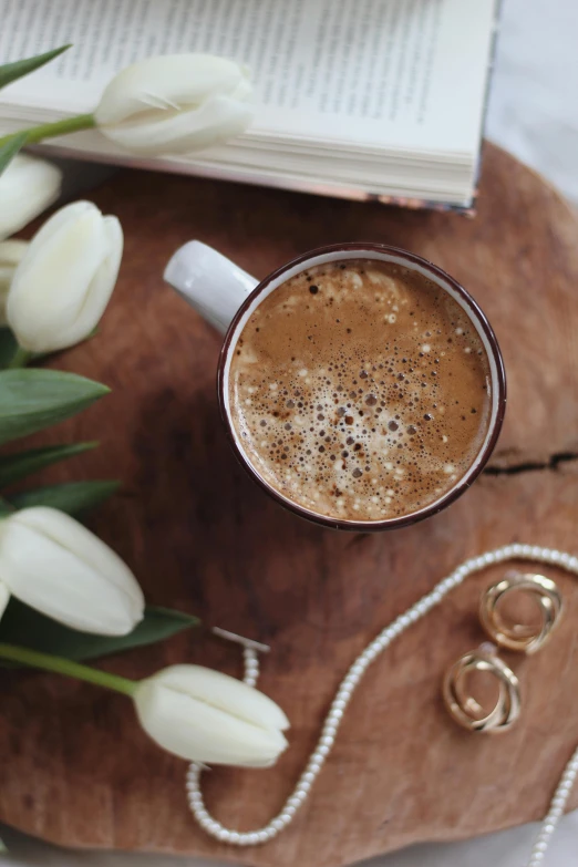 a cup of coffee sitting on top of a wooden tray, by Lucia Peka, trending on pexels, romanticism, tulips, gold and pearl necklaces, long coffee brown hair, brown and white color scheme