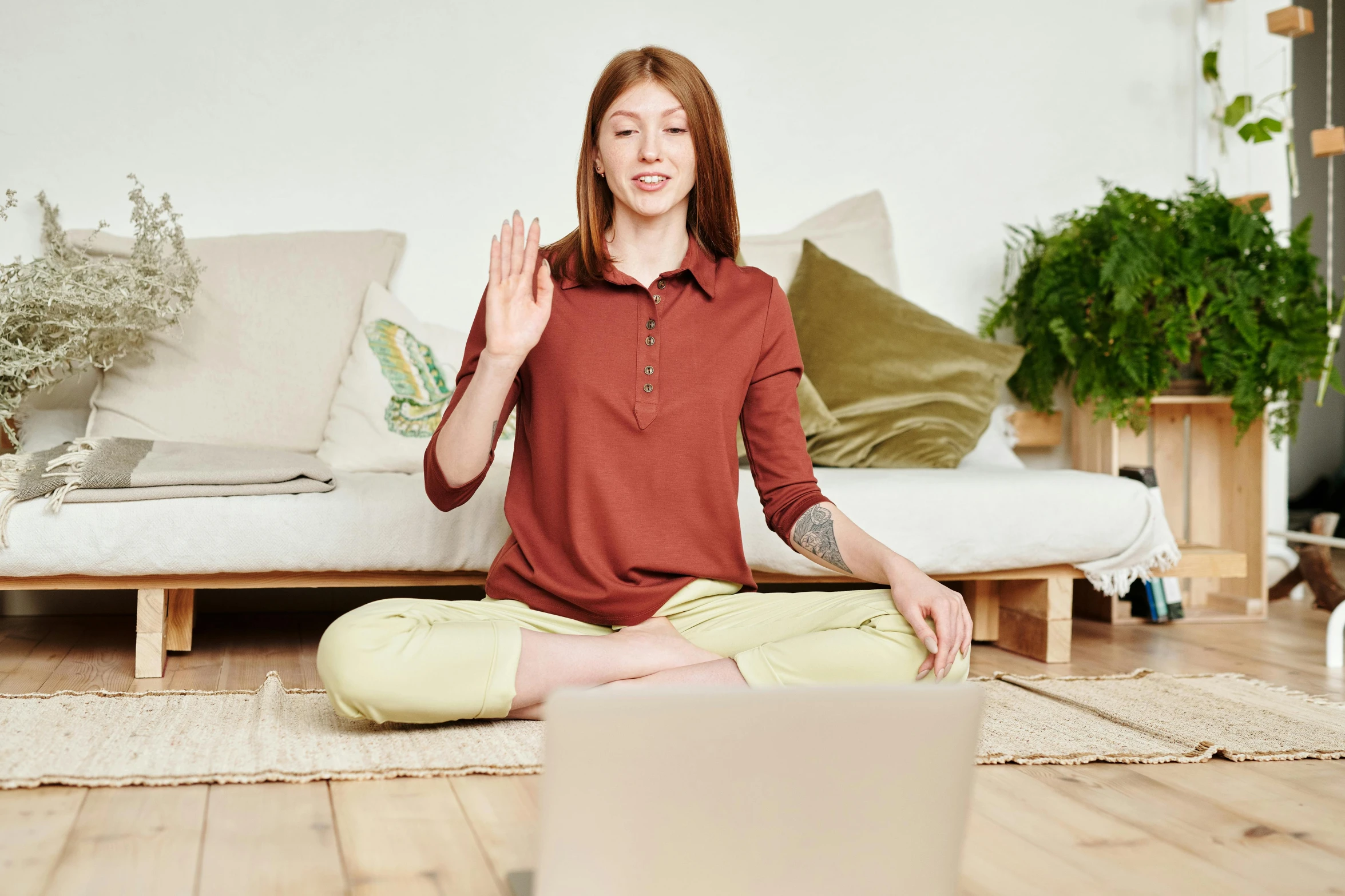 a woman sitting on the floor in front of a laptop, by Julia Pishtar, trending on pexels, figuration libre, red shirt brown pants, greeting hand on head, sukhasana, sitting on a couch