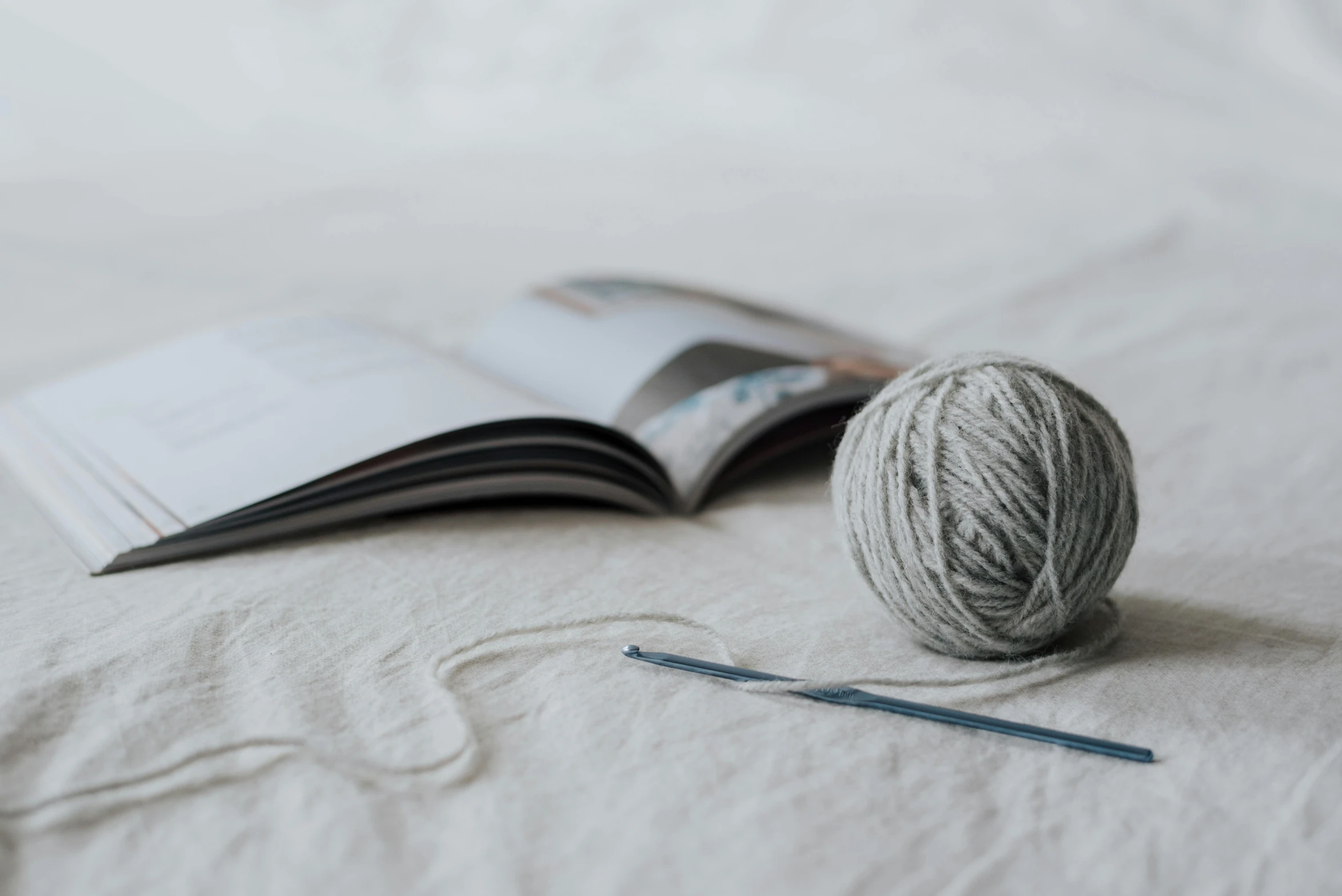 a ball of yarn sitting on top of a bed next to an open book, by Sylvia Wishart, unsplash, light grey, magazine pages, linen canvas, modeled