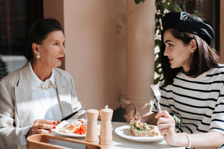 two women sitting at a table with plates of food, by Julia Pishtar, pexels contest winner, wearing a french beret, looks like audrey hepburn, 15081959 21121991 01012000 4k, family friendly