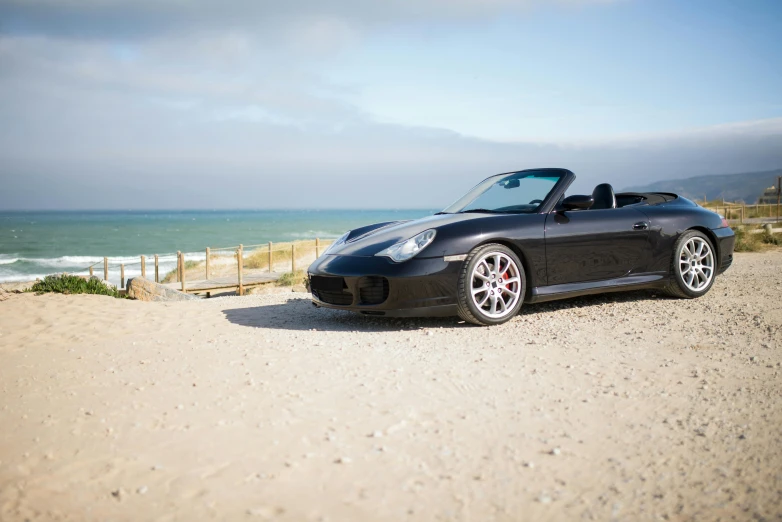 a black sports car parked on top of a sandy beach, a portrait, unsplash, normandy, 2 0 0 0's photo, porche, 4k”