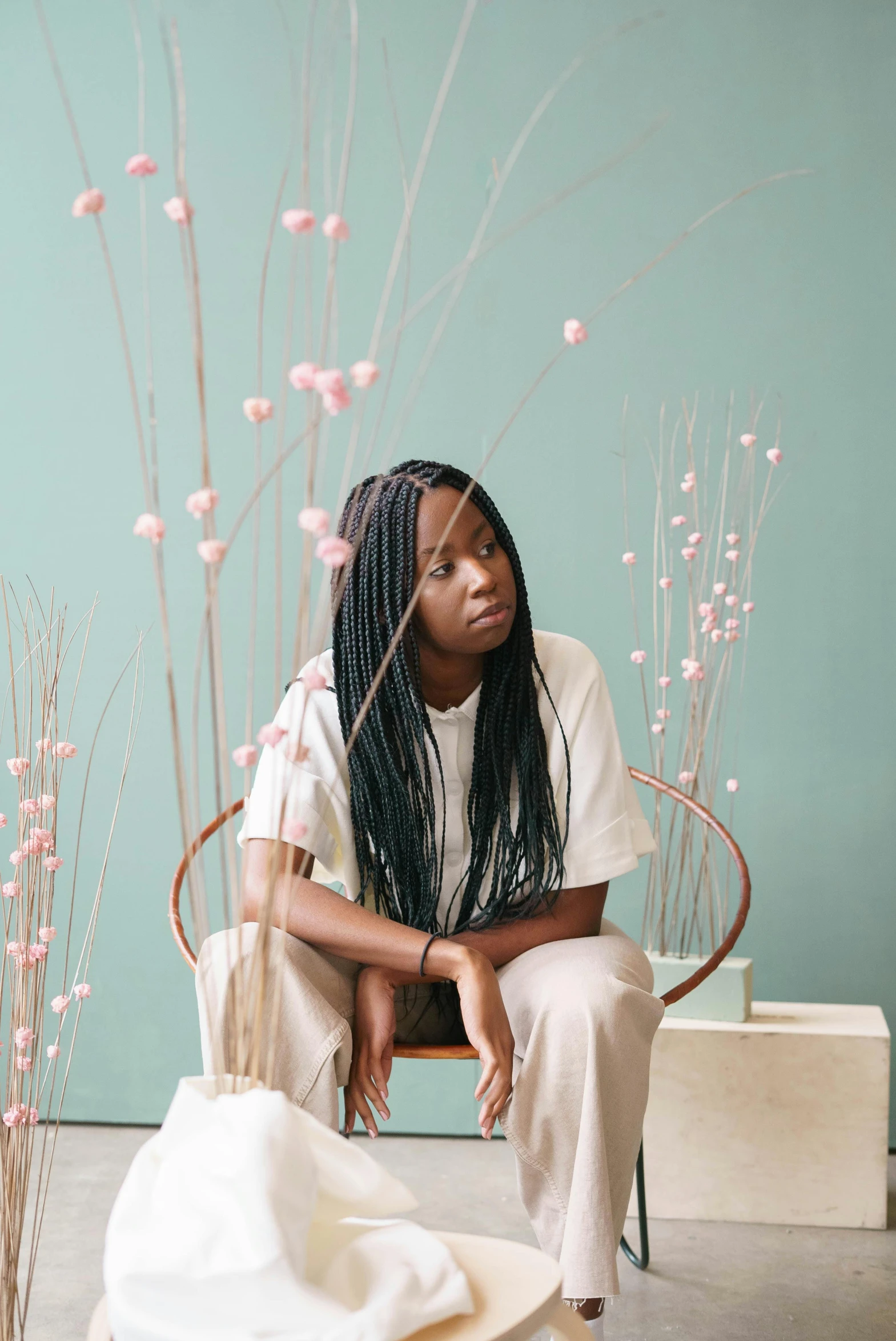 a woman sitting on a chair in a room, by Dulah Marie Evans, long black braided hair, willow plant, maria borges, teal studio backdrop