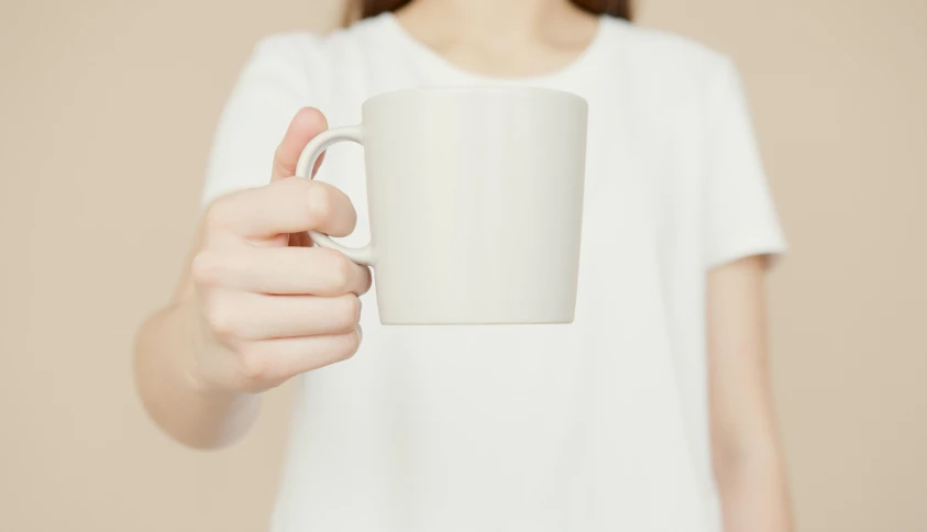 a woman holding a white coffee mug in her hand, by Nina Hamnett, minimalism, matte finish, white, low detail, cast