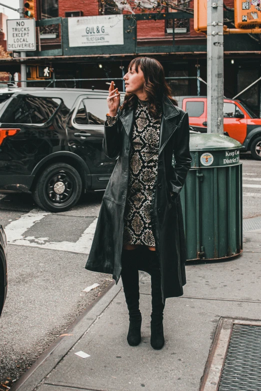 a woman talking on a cell phone on a city street, a photo, trending on pexels, baroque, leather trench coat, humans of new york style, snake skin, dramatic smoking pose