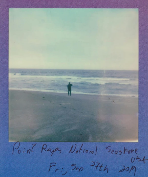 a man standing on top of a beach next to the ocean, a polaroid photo, volumeric ghostly rays, front label, ((purple)), ray