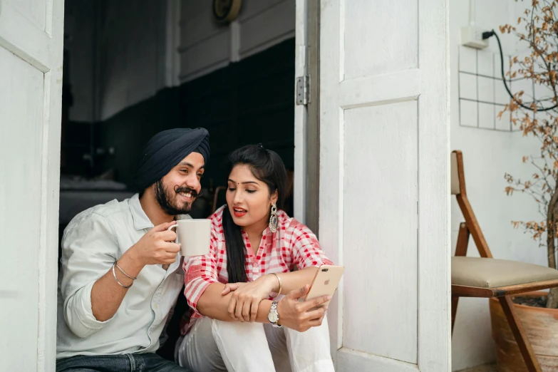 a man and woman sitting on a porch looking at a tablet, a picture, inspired by Manjit Bawa, pexels contest winner, with a white mug, leaning on door, everyone having fun, couple pose