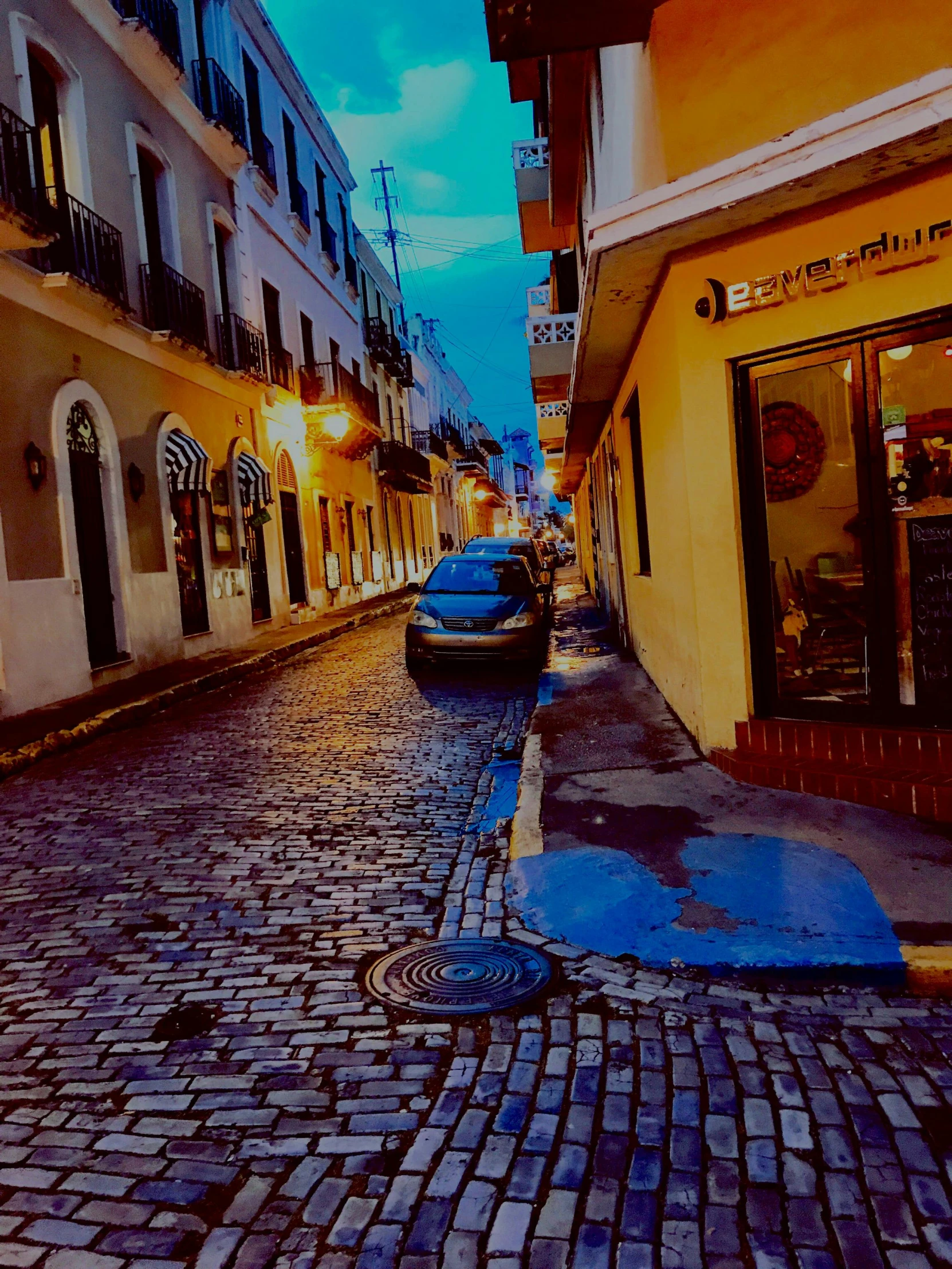 a row of parked cars on a cobblestone street, an album cover, by Robbie Trevino, pexels contest winner, puerto rico, calm evening, lo fi colors, vibrant but dreary blue