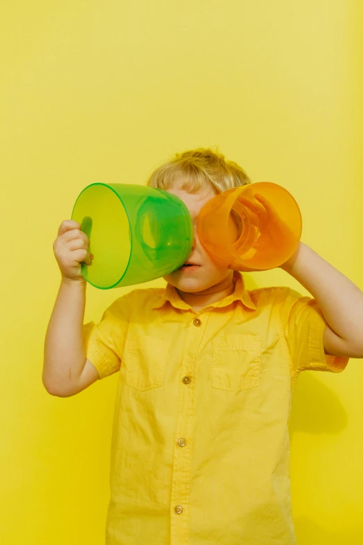 a young boy holding two cups in front of his face, by Doug Ohlson, pexels, colors: yellow, multiple stories, pastel', binoculars