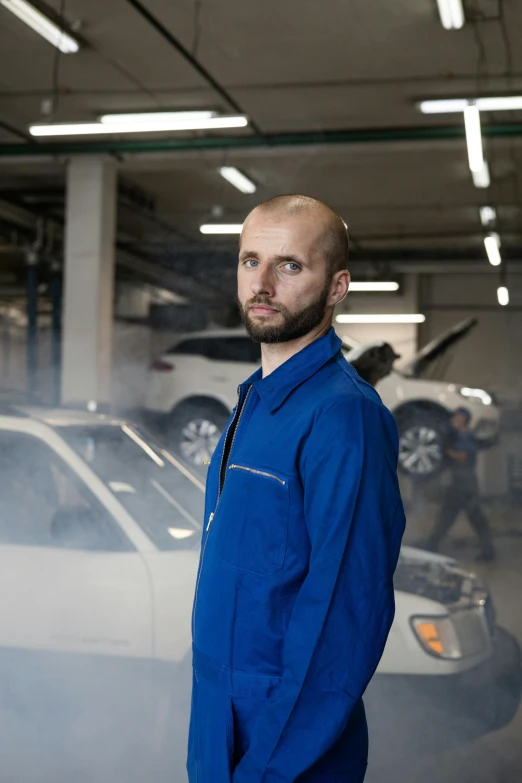 a man standing in front of a car in a garage, a portrait, inspired by Jakub Husnik, wearing blue jacket, performance, avatar image, mechanics