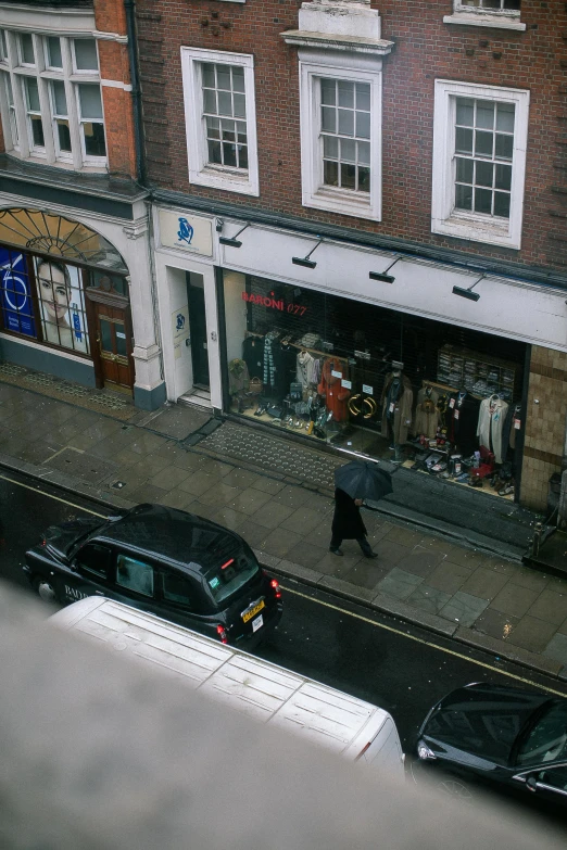 a person walking down a street with an umbrella, shop front, view from high, early 2 0 0 0 s, illustrious clothes