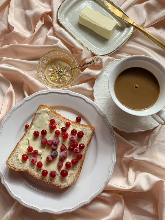 a white plate topped with a piece of bread next to a cup of coffee, a still life, by Henriette Grindat, trending on instagram, romanticism, cherry explosion, 🎀 🧟 🍓 🧚, gif, creamy skin