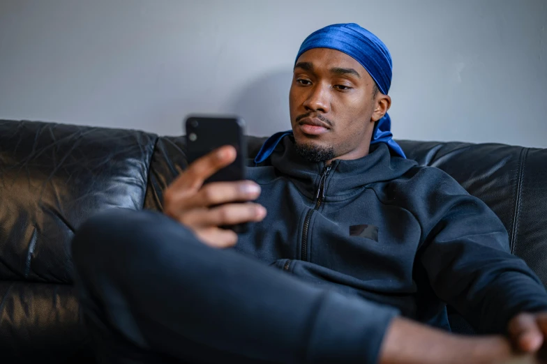 a man sitting on a couch holding a cell phone, a portrait, inspired by Terrell James, trending on pexels, dark blue beanie, kobe bryant, video game dunkey, looking content