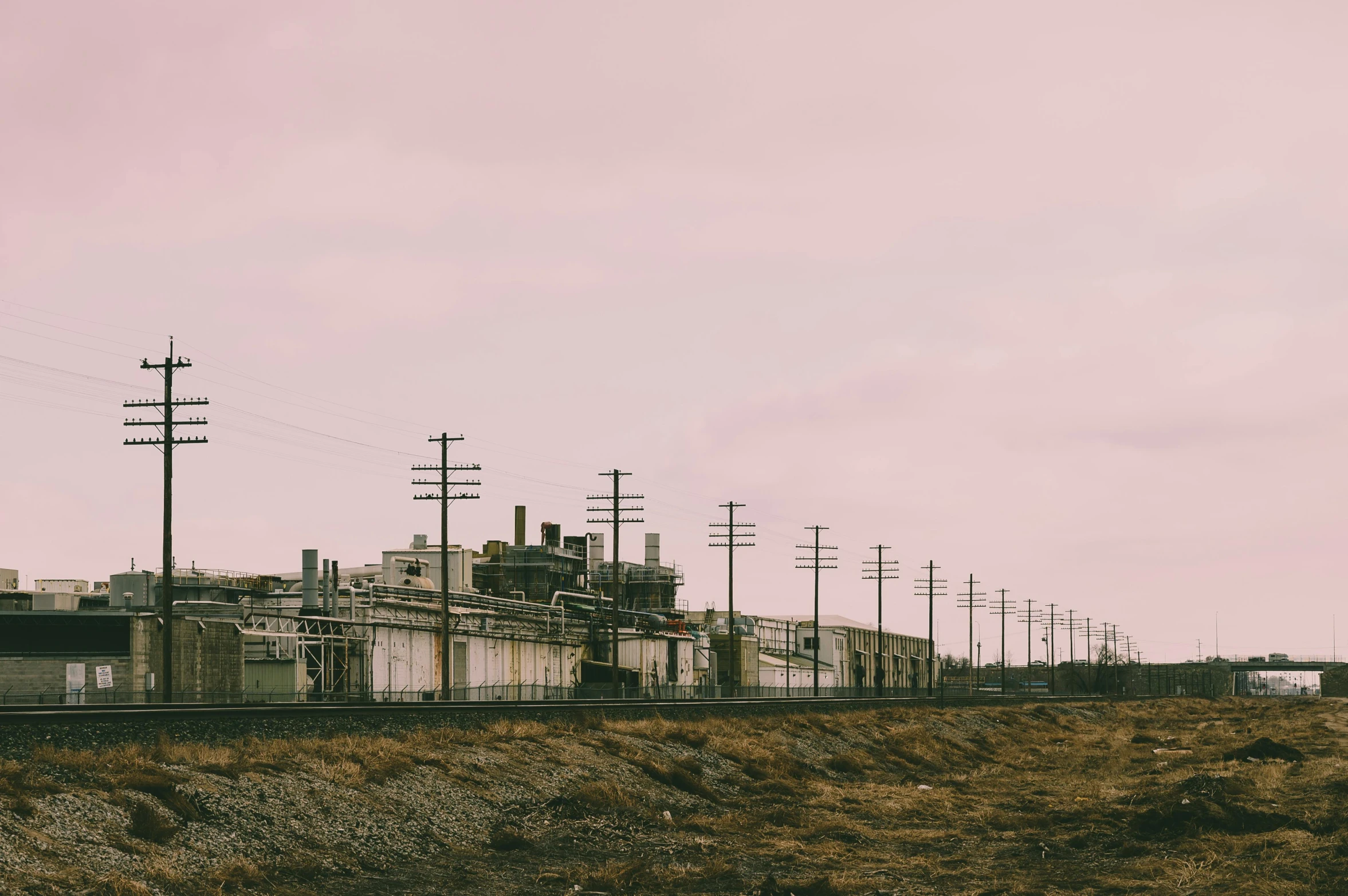 a train traveling down train tracks next to a field, a colorized photo, unsplash, brutalism, biroremediation plant, pink, oilfield scene, gloomy skies