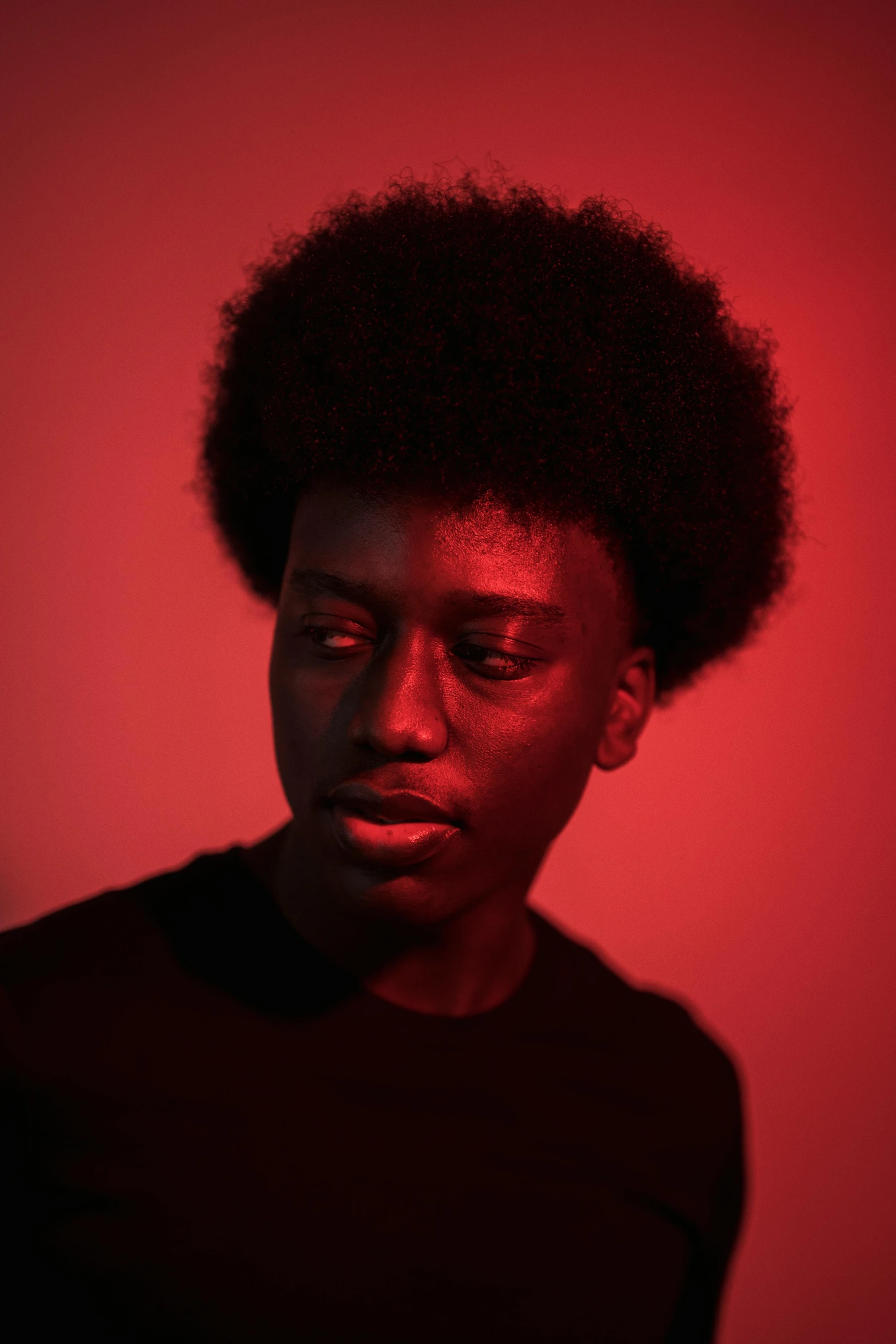 a man standing in front of a red wall, pexels contest winner, black arts movement, androgynous face, red glow, black on black, curls on top of his head