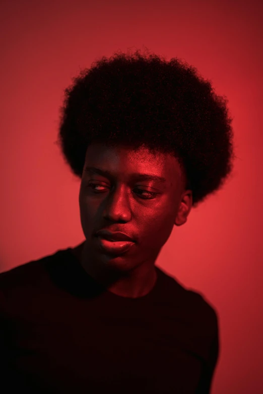 a man standing in front of a red wall, pexels contest winner, black arts movement, androgynous face, red glow, black on black, curls on top of his head