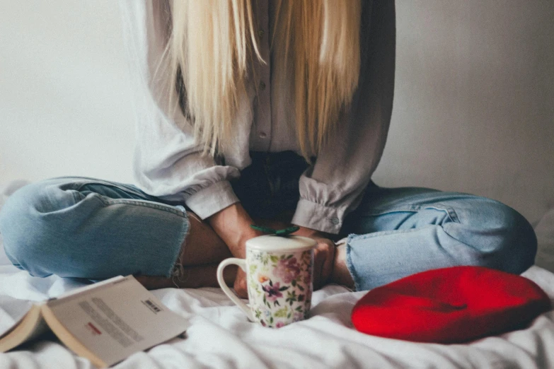 a woman sitting on a bed with a cup of coffee, inspired by Louisa Matthíasdóttir, trending on pexels, long straight blonde hair, best friends, android 18, slightly red