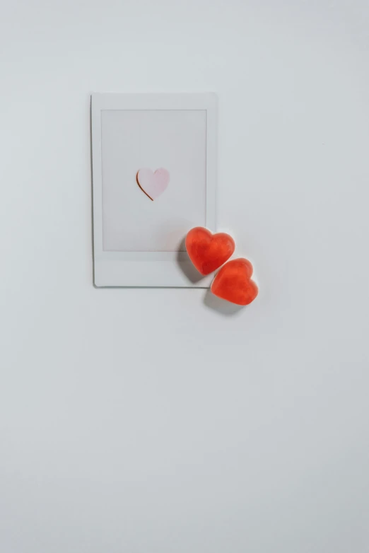 a couple of red hearts sitting on top of a white table, a polaroid photo, by Valentine Hugo, visual art, ( ( photograph ) ), made of glazed, eero aarnio, high angle close up shot