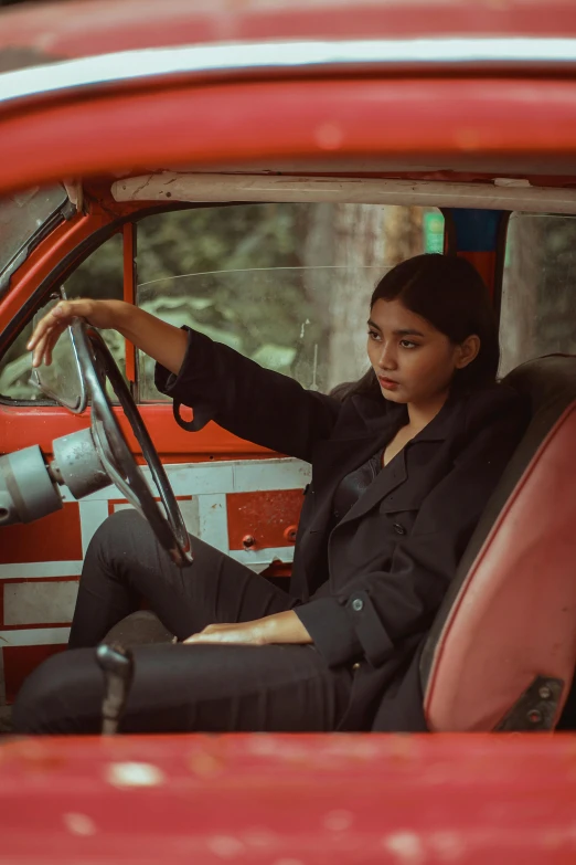 a woman sitting in the driver's seat of a red car, inspired by Elsa Bleda, pexels contest winner, sumatraism, wearing causal black suits, square, handsome girl, artisanal art