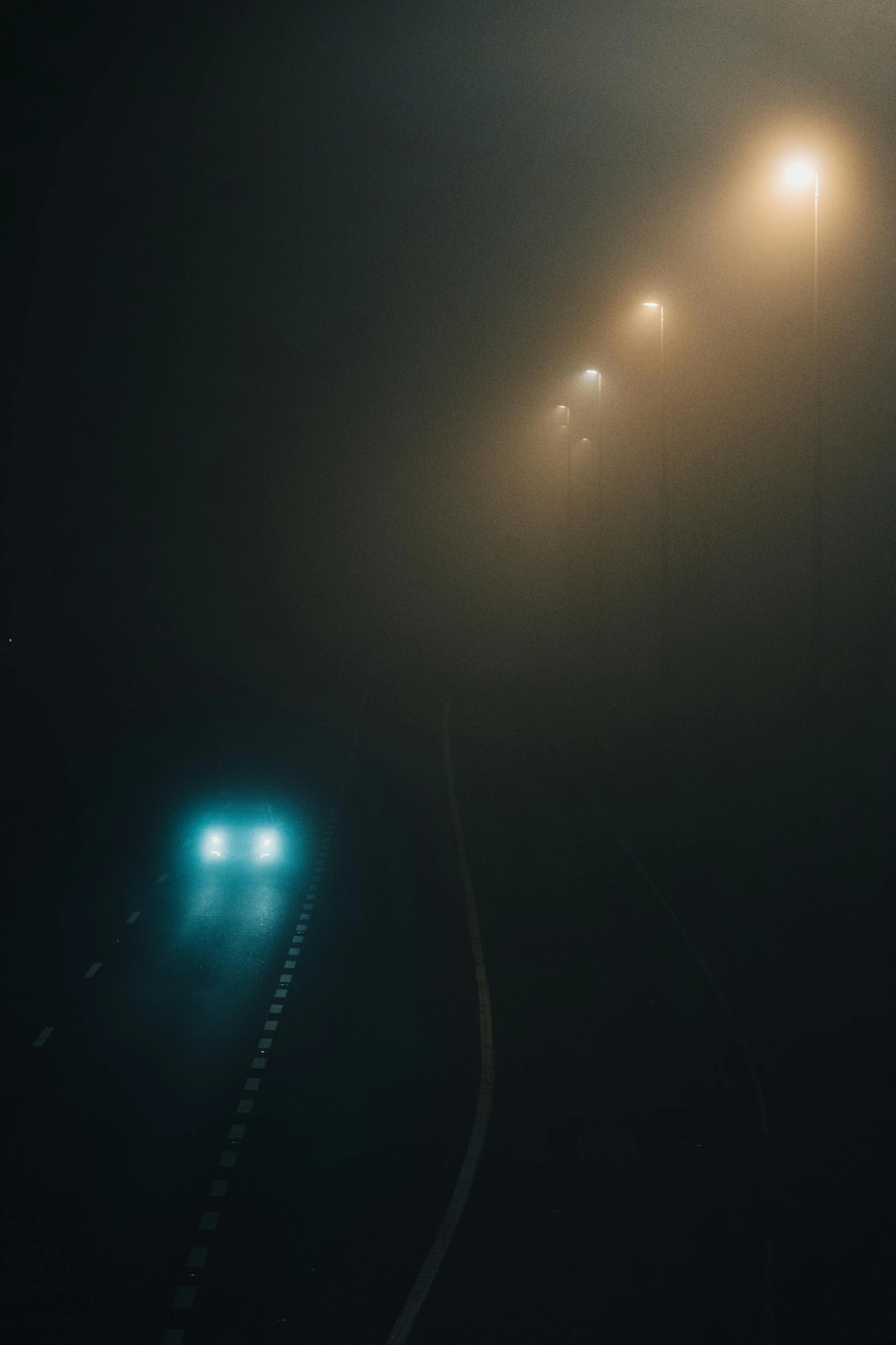 a couple of lights that are on in the dark, a picture, inspired by Elsa Bleda, unsplash contest winner, tonalism, car on highway, dense volumetric fog, cyan fog, unsettling creepy liminal space