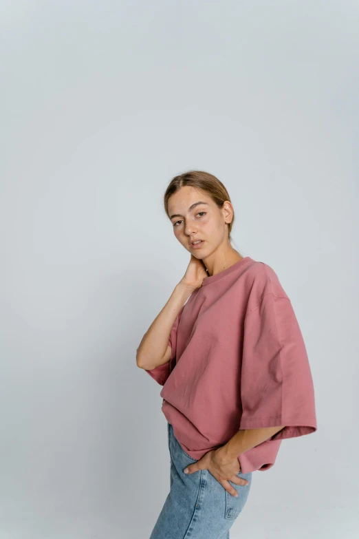 a woman wearing a pink top and jeans, by Tobias Stimmer, trending on unsplash, happening, in front of white back drop, dolman, cropped wide sleeve, looking to the side